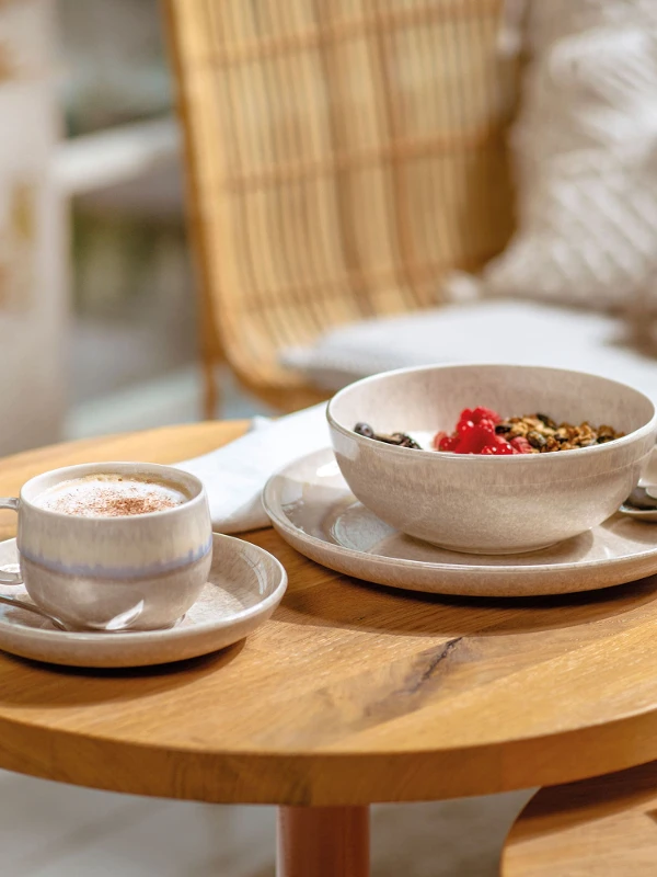 Eine Perlemor Tasse mit Kaffee und eine Schüssel mit Müsli auf einem Holztisch.