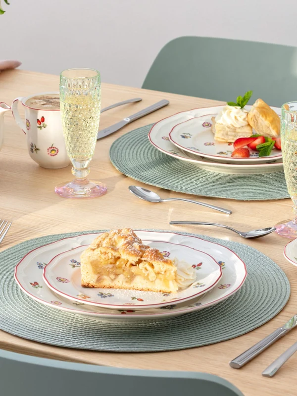 Ein gedeckter Tisch für zwei Personen mit Desserttellern, Teetassen, einer Teekanne, Sektgläsern und blumengemustertem Porzellan von Petite Fleur.