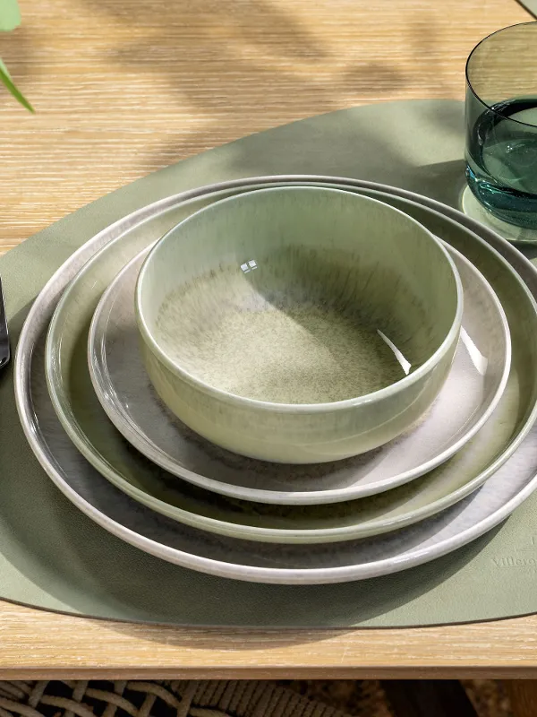 Een gedekte tafel met groen en beige servies, een kom, een glas, bestek en een groene placemat.