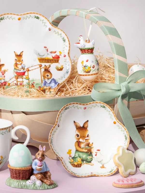 Un panier décoratif Annual Easter Edition 2026 avec des assiettes à thème lapin, une tasse, une figurine, des biscuits, des œufs et un ruban vert.