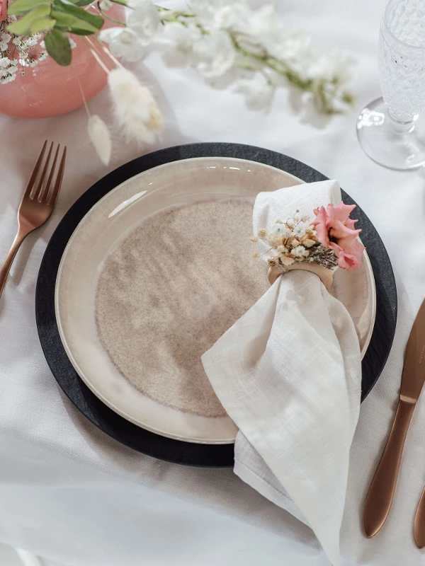 A table setting with Villeroy & Boch beige Perlemor dinner plate, copper-colored Manufacture flatware and flowers.