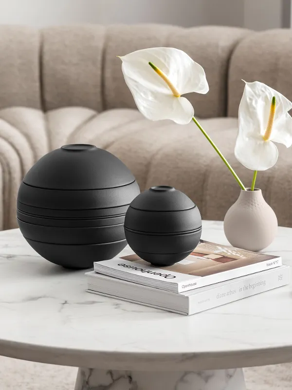 A beige coffee table with the black La Boule in 2 sizes in front of a beige sofa with a white blanket.