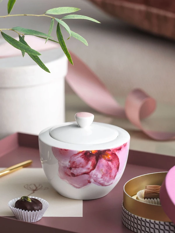 A Rose Garden sugar bowl with a candle, a golden spoon, a chocolate truffle and decorative items on a tray.