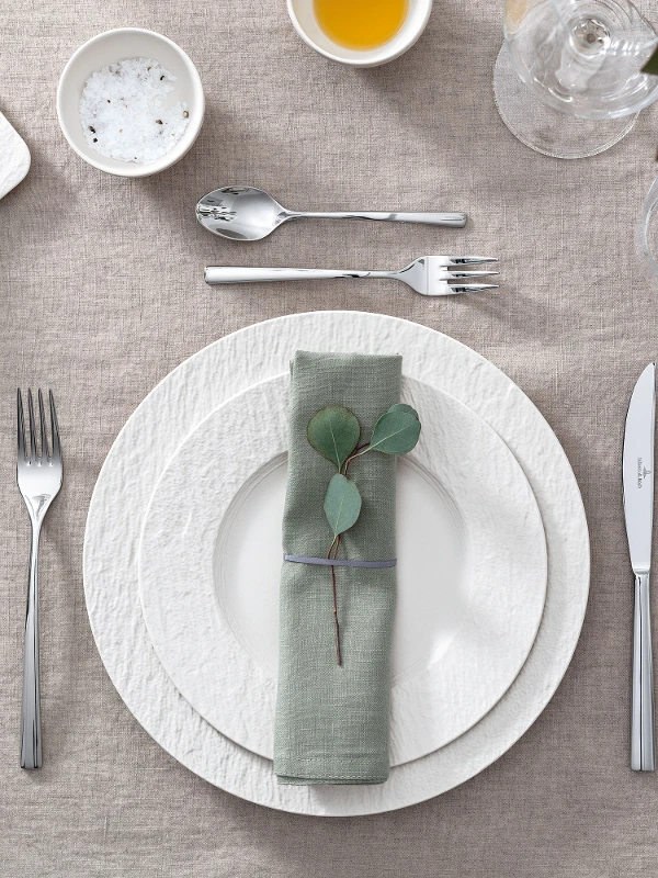 Une table dressée avec des assiettes Manufacture blanches de Villeroy & Boch ainsi que des feuilles d’eucalyptus et des couverts de table.