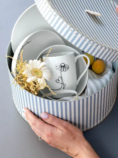 En rund eske med et Statement-bestikksett med blomstermotiv fra Villeroy & Boch og en tørkeklut, prestekrager og aprikoser som gave.