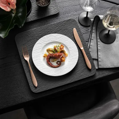 Elegante eetkamer met gastronomisch gerechten, wijn en modern Manufacture-servies in zwart en wit op een donkere houten tafel.