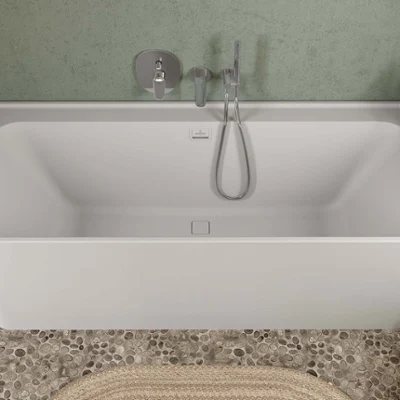 Une salle de bains moderne avec un plan double Collaro en bois clair et une vasque à poser Antao verte, un grand miroir rectangulaire et une armoire haute Collaro assortie. Un sol en galets et un décor minimaliste complètent le look.