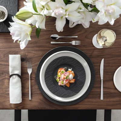 Décoration de table élégante avec un plat de fruits de mer sur des assiettes Manufacture, des fleurs blanches, un verre de vin blanc et une petite assiette avec des tranches de citron.