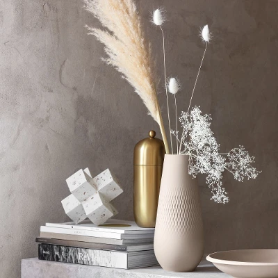 A table with a beige Manufacture vase and a NewMoon plate on it.