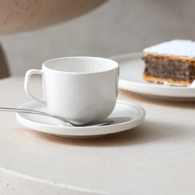 Tazza e piattino da caffè Afina bianchi di Villeroy & Boch con torta sullo sfondo.