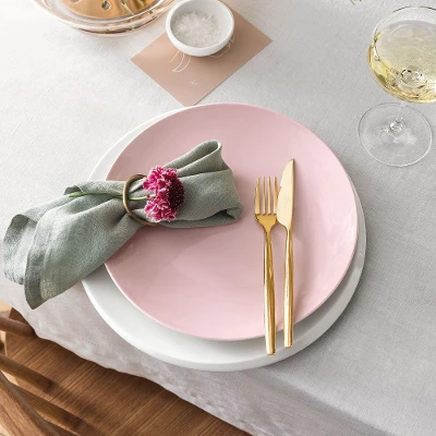 A set table with a pink Rose Garden plate, white NewMoon plate and gold MetroChic flatware.