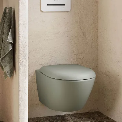 Badewanne im Boho-Stil Eine moderne weiße Collaro Badewanne mit verchromter Armatur in einem Badezimmer mit Kieselsteinboden, einem Weidenkorb und einem gewebten Teppich. Links neben einem Fenster steht eine Topfpflanze.