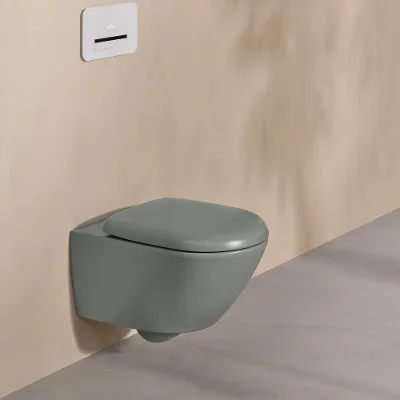 Et Villeroy & Boch WC fra Antao-kolleksjonen i grønt med hvitt betjeningspanel på en naturfarget vegg.