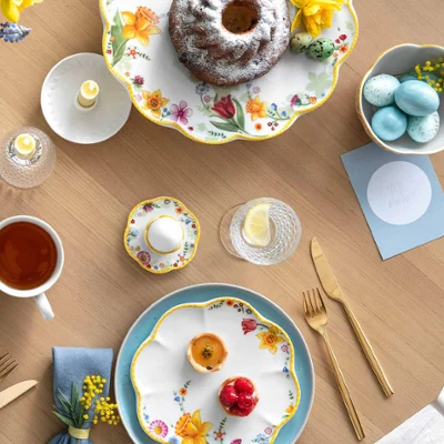 Une table printanière décorée avec de la vaisselle Spring Awakening et Crafted, un kouglof, un plat creux rempli de flocons d’avoine avec des baies, une tasse de thé et des œufs décoratifs.