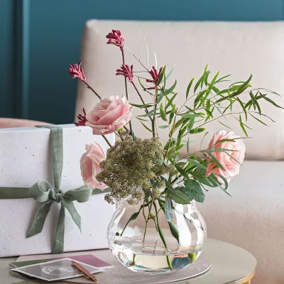 Een Rose Garden vaas met roze bloemen en een cadeautje op een tafel.