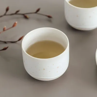 Deux tasses Winter Glow avec un motif d’étoiles, plus une assiette avec des biscuits et des branches décoratives sur un fond beige.