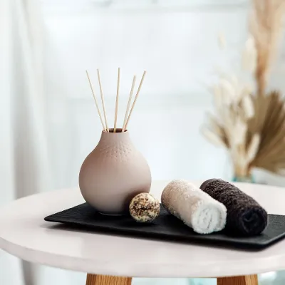 Beige Manufacture Vase mit Duftstäbchen auf einem Tablett mit Handtüchern.