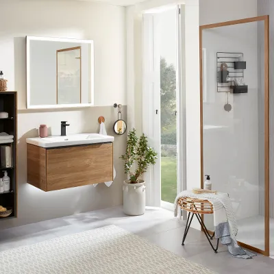 Bagno moderno con mobile lavabo in legno, pensili, cabina doccia con parete in vetro e ampia finestra con luce naturale. Sul pavimento c’è un tappeto e gli utensili da bagno sono appoggiati su un piccolo sgabello.