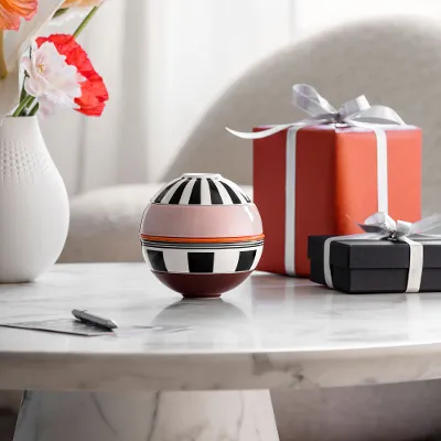 La petite Boule Memphis and two wrapped gifts stand on a table. La petite Boule Memphis from Villeroy & Boch and two wrapped gifts stand on a marble table, with a vase of flowers in the background.