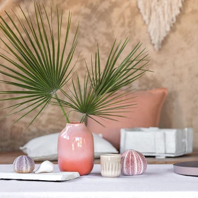 A table with a Perlemor vase and scented candle from like. by Villeroy & Boch with shells on it.