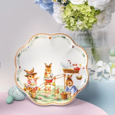 Assiette décorative Annual Easter Edition avec illustrations d’animaux, exposée parmi des vases de fleurs et des œufs aux couleurs pastel sur une table.