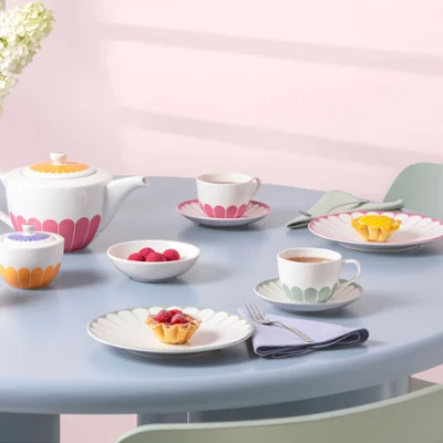 Un servizio da tè dai colori pastello con tazze, piattini, piatti con motivi floreali colorati della collezione Fleur e piccoli dessert su un tavolo rotondo azzurro.