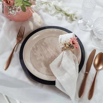 A table setting with Villeroy & Boch beige Perlemor dinner plate, copper-colored Manufacture flatware and flowers.