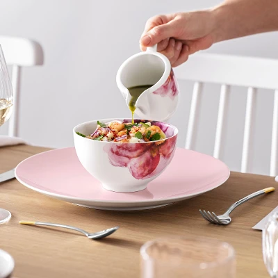 Een persoon giet dressing op een salade in een Rose Garden schaal aan een elegant gedekte eettafel met Rose Garden servies.