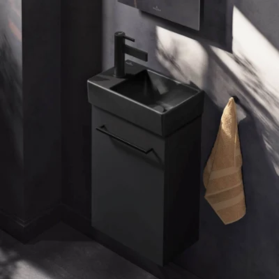 Une salle de bains moderne avec un plan de toilette Collaro noir éclairé, une vasque Antao noire mate, un miroir rond More to See Lite et des objets de décoration.