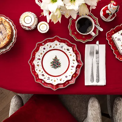Toy's Delight collection on a laid table Festively laid table with red tablecloth, Christmas plate, cake, coffee and cutlery on a napkin.
