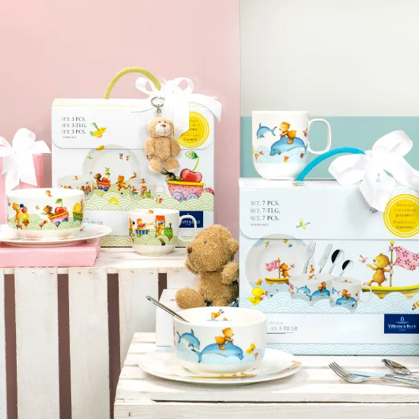 Des articles cadeaux et un ensemble de vaisselle pour enfants Happy as a bear et Hungry as a bear sur une table avec un fond pastel.