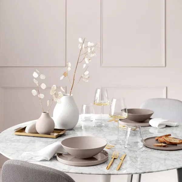 Une table de couleur blanche dressée avec La Boule Pure Beige ainsi que des verres à vin MetroChic et un vase contenant des fleurs.