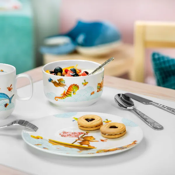 Une présentation de petit-déjeuner avec une salade de fruits, des biscuits sur une assiette et deux tasses de vaisselle pour enfants Happy as a bear sur une table.