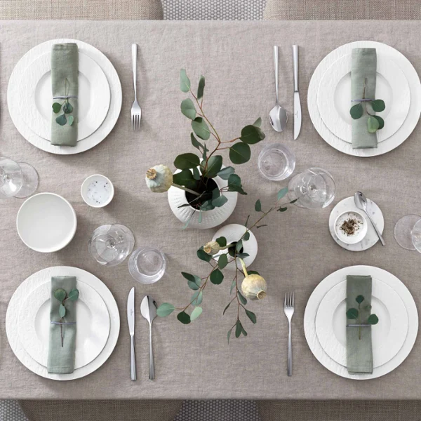 Elegantly laid dining table with harmonious, white Manufacture crockery and glasses Elegantly set dining table with matching crockery and glasses from the Manufacture collection in white and a simple green and white centrepiece.