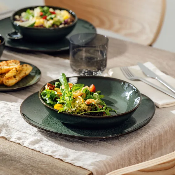 Ein stilvoll gedeckter Tisch mit Lave Vert Geschirr – ein grüner Speiseteller, eine passende Schale und frischer Salat – die perfekte Kombination aus handgefertigtem Design.