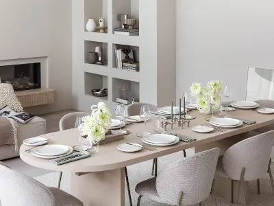 Vue latérale d’une table dressée avec de la vaisselle Afina et des couverts de table Piemont dans une pièce beige.