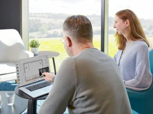 Espace de travail avec deux personnes Deux personnes sont assises devant un ordinateur portable. L'homme pointe l'écran.