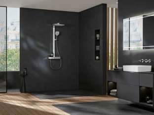 Une salle de bains avec douche à l’italienne Infinity Shower de Villeroy & Boch Une salle de bains moderne avec des murs sombres, une douche à l’italienne, un miroir rectangulaire, un lavabo sur un plan de toilette suspendu et une fenêtre avec vue sur la ville. Le sol est composé d’un mélange de bois et de carrelage.