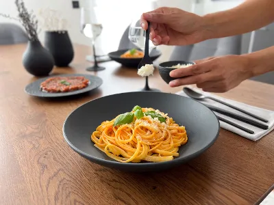Spicy pasta in Manufacture bowl with wine glasses At a modern dining table, pasta is garnished with cheese in a Manufacture Pasta bowl, while wine glasses can be seen in the background.