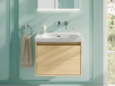 Toalla beige en un lavabo en un baño verde Baño moderno con un mueble de lavabo de madera clara, un lavabo blanco, un espejo de pared y una toalla colgada de un aro metálico frente a una pared verde menta.