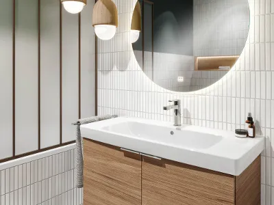 Architectura washbasin on wooden washstand with a round mirror Modern bathroom with a large round mirror, an Architectura washbasin on a wooden washstand, hanging pendant lights and white tiled walls.