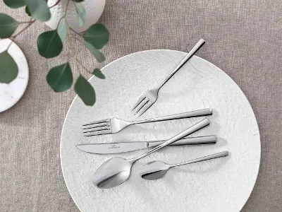 Piemont flatware with white Manufacture plate on neutral table cloth Elegant table decor with modern Piemont flatware and decorative green on a neutral table cloth.