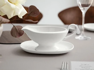 Royal gravy boat on a light-colored tabletop Elegant white Villeroy & Boch sauce boat from the Royal collection on a light tablecloth next to a stylish floral arrangement.