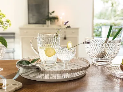 Glasses from Villeroy & Boch with lemon water stand on a tray on a wooden table with glass bowls and a napkin.