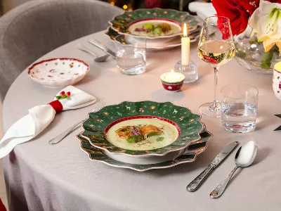 Toys Delight imbandita a festa per Natale Una tavola imbandita a festa con una ciotola di zuppa, pane, posate, candele, un bicchiere di vino e decorazioni natalizie.