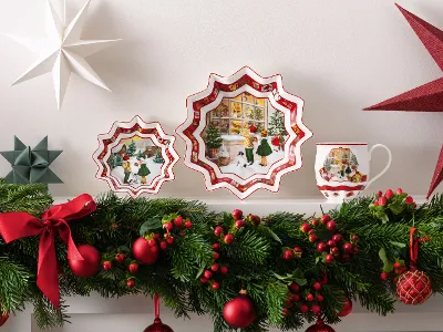 Toy’s Fantasy collection from Villeroy & Boch Toy’s Fantasy collection from Villeroy & Boch, a decorative plate, a mug decorated with winter landscapes, star-shaped ornaments, and a lush garland decorated with red ribbons and berries on the mantelpiece.