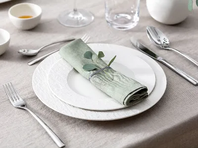White Manufacture plate with napkin on a table A set table with two white Manufacture plates, pastel green napkin, Piemont flatware and eucalyptus.