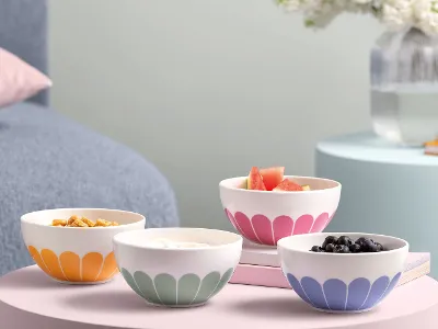 Villeroy & Boch Fleur bowls with various foods placed on pastel-colored tables next to books and a vase with flowers.