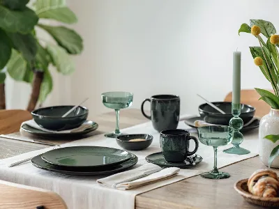 A Dining Table Set with Lave Green A dining table with green tableware, glassware, cutlery, a candle, and a vase with yellow flowers.