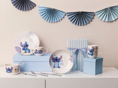 Ein Platzdeckchen-Set mit Geschirr, Tassen und Schalen zum Thema "Stitch" auf blauen Boxen, mit gestreifter Geschenkbox und Dekoration.